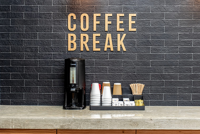 Coffee station with drip coffee machine, cups, stir sticks, creamer. and sugar.