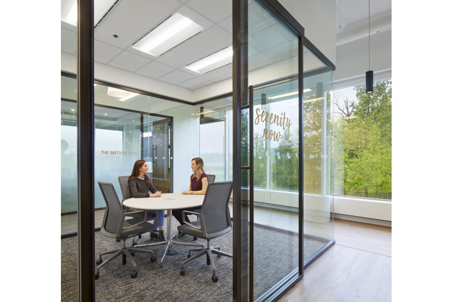 A meeting is taking place between two individuals at a conference table located in a room with architectural glass walls.