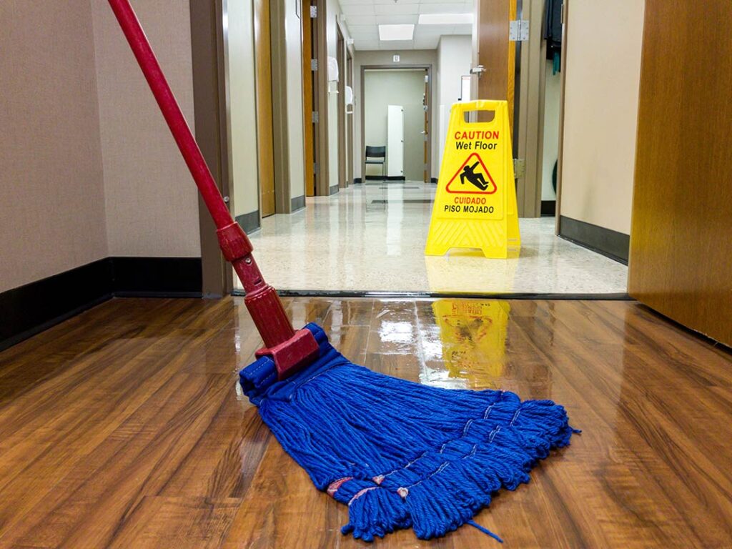 Wet mop cleaning floor with caution sign in the backgroud.